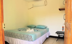 A small, single-bed room with a patterned bedspread, a single pillow, and a bench.