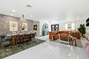 A modern living room with a dining area, featuring a stone wall, a sofa, a coffee table, and a large plant. - Mins to Beach • Backyard Oasis • Heated Pool & Spa (West Palm Beach)