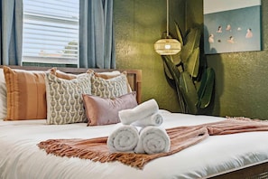 A neatly made bed with rolled towels, patterned pillows, a woven light fixture, and a wall art piece. - Mins to Beach • Backyard Oasis • Heated Pool & Spa (West Palm Beach)