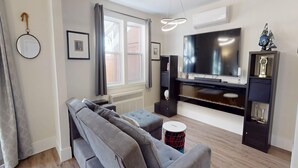 Een woonkamer met een bank, een televisie, een open haard en een radiator.