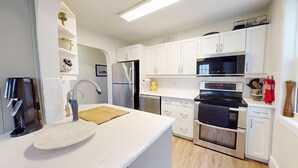 Een moderne keuken met witte kasten, roestvrijstalen apparatuur, een houten aanrechtblad en een inbouwoven.