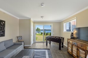 Un salón con sofá, mesa de fútbol, televisor y vista a un lago a través de un ventanal.