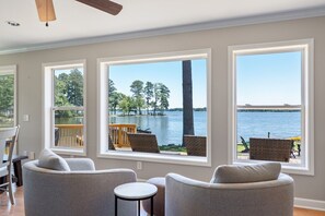 Una habitación con ventanas amplias que ofrecen vistas a un lago y árboles. Hay dos sillas y una mesita.