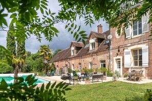 Une maison traditionnelle en briques, dotée d’une piscine, d’un espace extérieur aménagé et d’une végétation luxuriante.