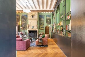 Une pièce dotée d’une cheminée, de bibliothèques et d’un coin salon avec un parquet en point de Hongrie.