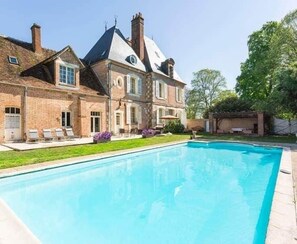 A large house with a swimming pool, a brick exterior, and a well-maintained lawn.