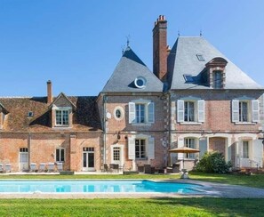 Une grande maison en briques avec une piscine, plusieurs cheminées et une pelouse bien entretenue.