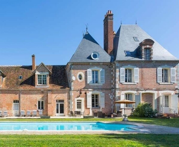 A large brick house with a swimming pool, multiple chimneys, and a well-maintained lawn.