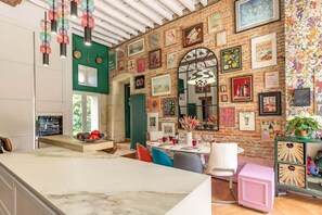 A modern kitchen with a marble countertop, a dining area with colorful chairs, and a brick wall adorned with various framed pictures and artwork.