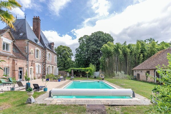 Uma casa grande de tijolos com piscina, área de estar ao ar livre e um jardim.