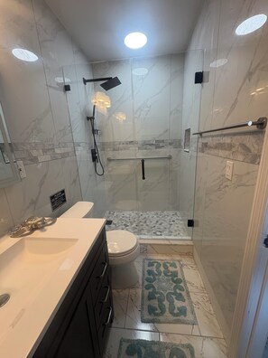Un baño moderno con ducha de vidrio, inodoro, lavamanos y espejo.