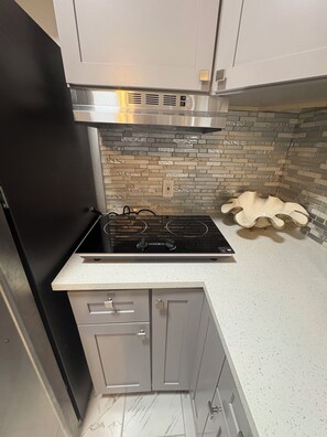 Una cocina compacta con estufa negra, gabinetes grises, salpicadero con azulejos estampados y piso de mármol.