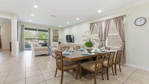 Un coin repas avec une table dressée pour quatre personnes, entourée de chaises, un téléviseur accroché au mur et une horloge.