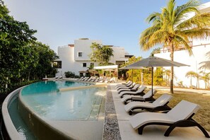 Ein Swimmingpool mit Liegestühlen und Sonnenschirmen, umgeben von Grünpflanzen und einem Gebäude im Hintergrund.