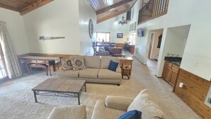 A spacious living room with a high ceiling, a dining area, and a kitchen in the background. - Munds Park Basecamp Cabin (Sedona)