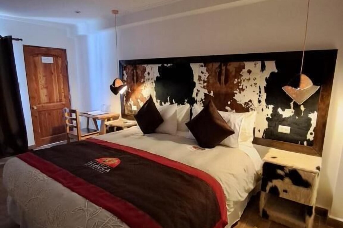 Ein Hotelzimmer mit einem großen Bett, einem Nachttisch, einer Lampe, einer Holztür und einem gemusterten Teppich.