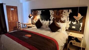 A hotel room with a large bed, a nightstand, a lamp, a wooden door, and a patterned rug.