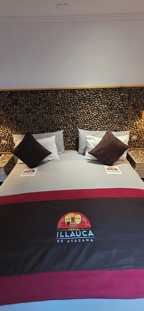 Uma cama com um logotipo, almofadas e uma parede de pedra ao fundo.