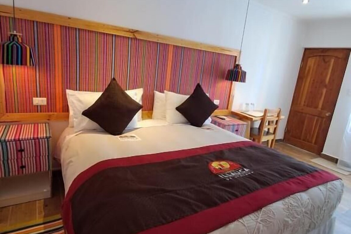 Ein Hotelzimmer mit einem Bett, einem Nachttisch, einem Sessel, einem Bücherregal und einer Holztür.