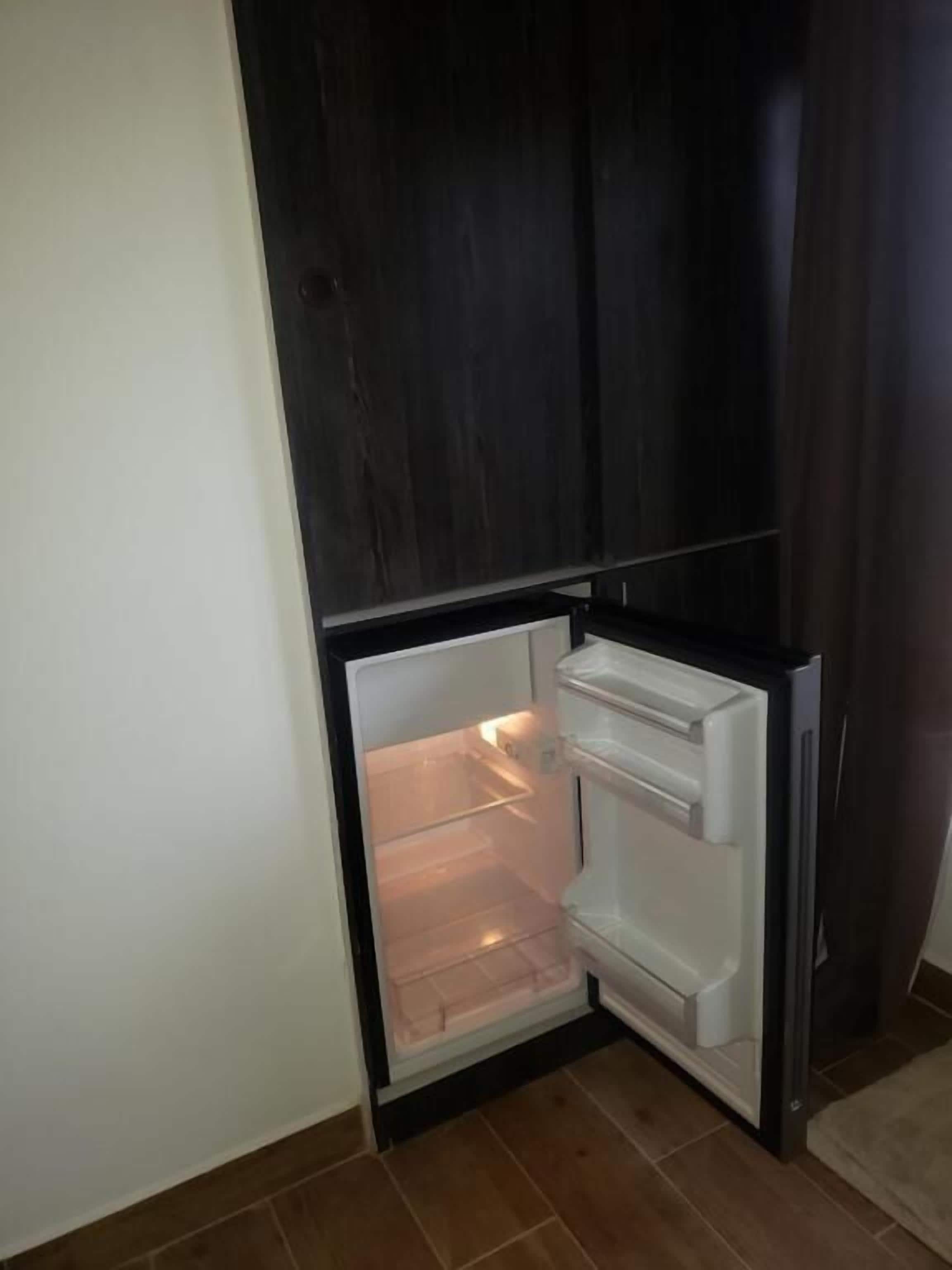 A corner of a room with a dark wooden cabinet and a white refrigerator with its door open.