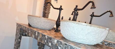 Un baño con tocador de mosaico de piedra, un espejo redondo y una lámpara con bombillas expuestas.