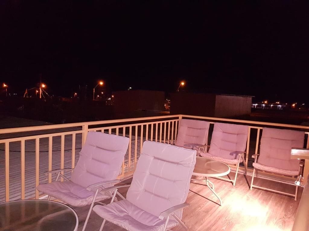 Une terrasse sur le toit, dotée de chaises longues et d’une table en verre, offrant une vue sur le paysage urbain illuminé la nuit.