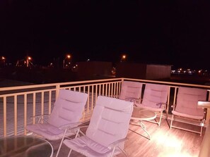 A rooftop terrace with lounge chairs and a glass table, overlooking a cityscape at night. - HOSTAL ILLAUCA DE ATACAMA  (San Pedro de Atacama)