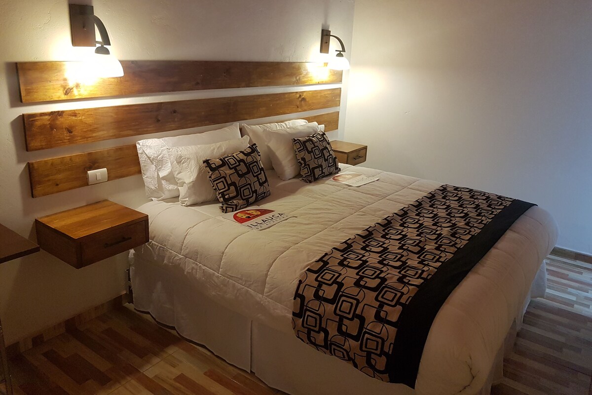 Ein ordentlich bezogenes Bett mit einem gemusterten Überwurf, zwei Nachttische mit Wandlampen und ein hölzernes Kopfteil.