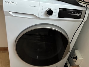 Una lavadora blanca con panel de control, una perilla y un cable de alimentación conectado.