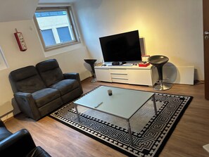Uma sala de estar com sofá, mesa de centro, televisão, abajur e tapete estampado.