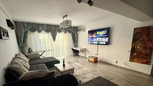 A living room with a sofa, a coffee table with wine glasses, a TV mounted on the wall, and a painting. - Cozy 2-bedroom apartment in tranquil Iași with AC (Iași)