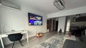 A modern living room with a flat-screen TV, a desk, a black chair, a grey sofa, and a patterned rug. - Cozy 2-bedroom apartment in tranquil Iași with AC (Iași)