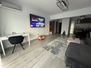 A modern living room with a flat-screen TV, a desk, a black chair, a grey sofa, and a patterned rug.