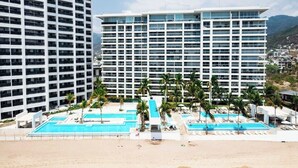 Ein Hotel mit mehreren Etagen, einem Poolbereich mit Palmen und Blick auf eine Berglandschaft.