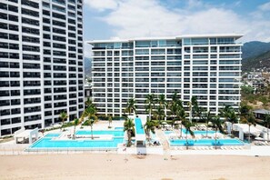 Um hotel com vários andares, área de piscina com palmeiras e vista para uma paisagem montanhosa.