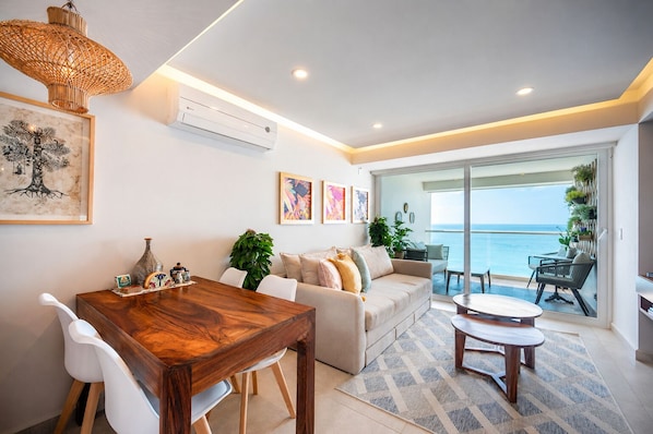 Uma sala de estar moderna com uma mesa de jantar de madeira, um sofá e uma varanda com vista para o mar.