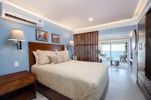 Quarto com uma cama grande, luminárias de cabeceira, ar condicionado e vista para o mar através de uma porta deslizante.