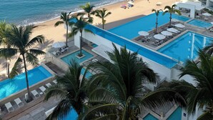 Ein Poolbereich mit Blick auf den Strand und den Ozean, mit Palmen und einem Hochhaus.