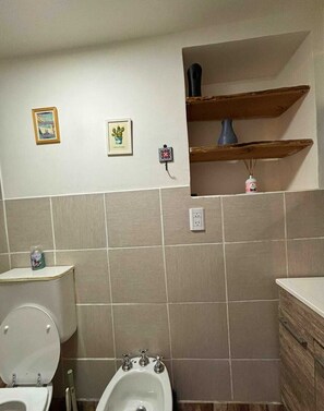 Un baño con inodoro, bidé, paredes con azulejos y dos cuadros enmarcados.