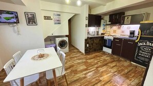 A compact kitchen with a washing machine, a dining area with a table and chairs, and a kitchen counter with a refrigerator and a Jack Daniel's whiskey sign.