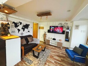Una sala de estar con un sofá, una mesa de centro, televisor, mapa del mundo y un sillón azul.