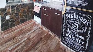 A kitchen with a stone backsplash, dark wooden cabinets, a stove, and a refrigerator with a Jack Daniel's label.