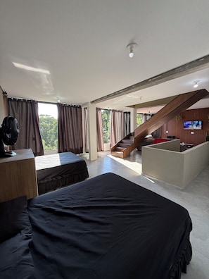 Ein Hotelzimmer mit Bett, Schreibtisch, Ventilator, Fernseher und einer Treppe, die zu einem Balkon führt.