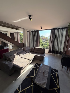 Ein modernes Wohnzimmer mit einer Eckcouch, einem Esstisch und Blick auf Grünflächen.