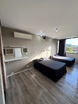 Ein Schlafzimmer mit zwei Betten, einem Deckenventilator, einer Klimaanlage und einem Fenster mit Blick auf Grünflächen.