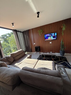 Ein modernes Wohnzimmer mit einer Couch, einem Couchtisch, einem Fernseher und einer Zimmerpflanze.