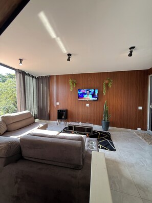Ein modernes Wohnzimmer mit einem großzügigen Ecksofa, einem flachbildfernseher an der Wand und einer Topfpflanze.