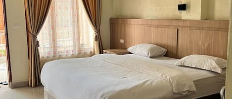 A hotel room with a large bed, a wooden headboard, a bedside table, and a window with curtains.