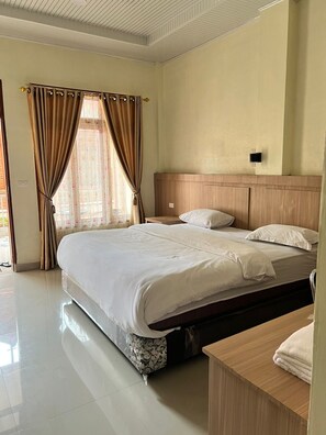 Une chambre d’hôtel avec un grand lit, une tête de lit en bois, une table de chevet et une fenêtre avec des rideaux.
