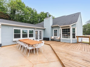 A house with a deck, a dining area with a table and chairs, and a garage.
